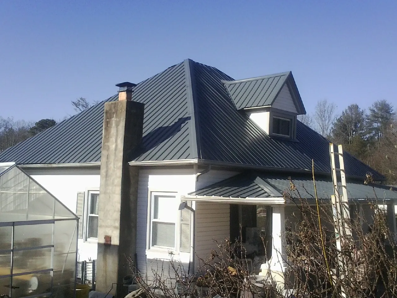 Dark blue standing seam metal roof on a white farmhouse with dormer — Slate & Tile Roof Repair by Roofing Brothers in Walker