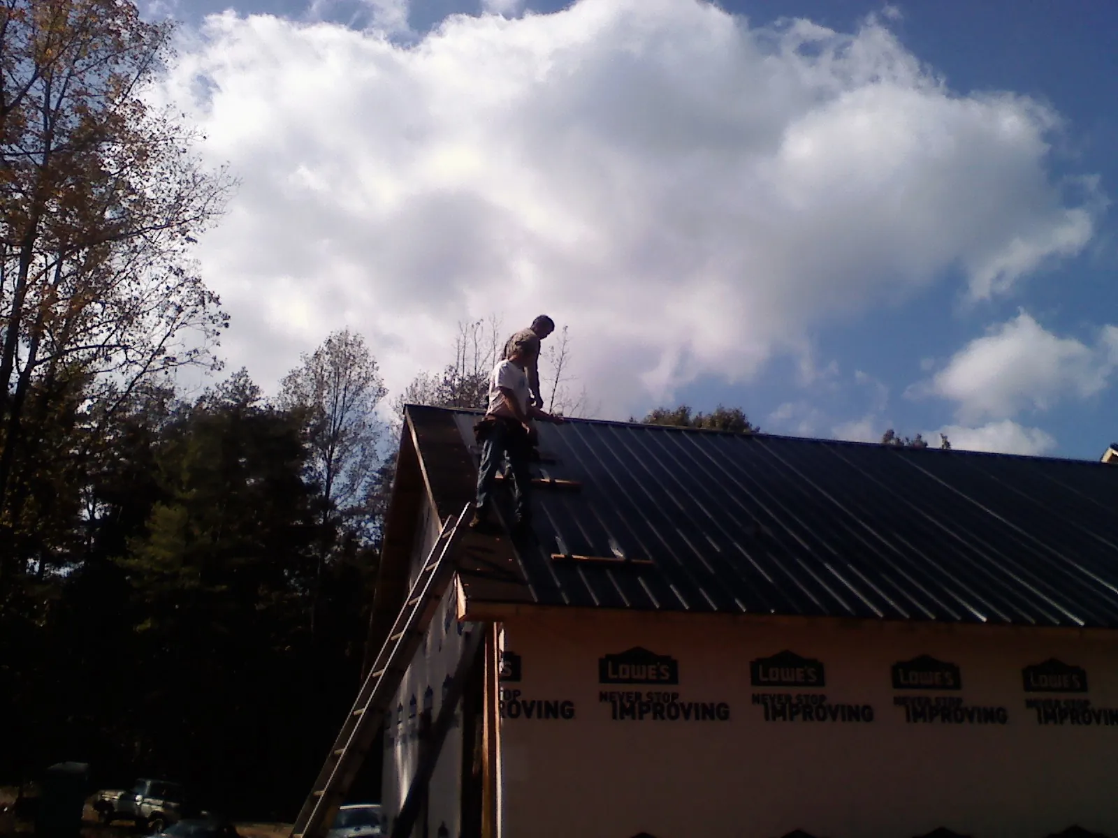 Roofer fastening dark metal panels high against a cloudy sky, from a Roof Inspection job in Walker